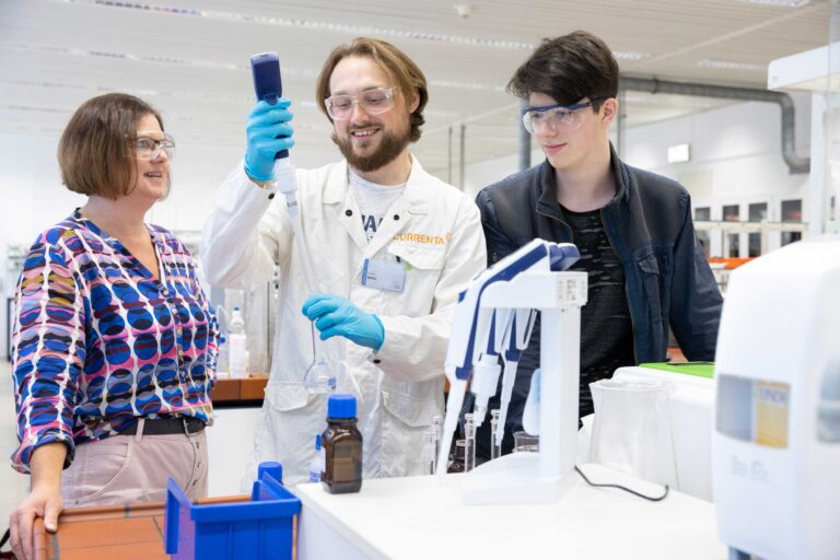 Drei Personen in einem Labor, Schülerpraktikant bekommt die Handhabung einer Pipette demonstriert